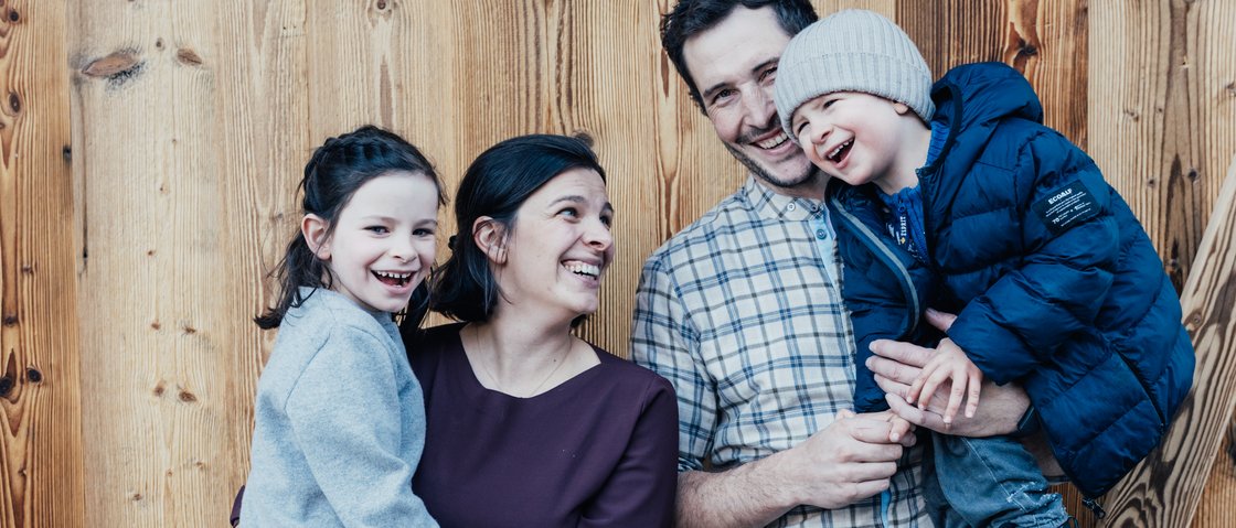 Warum Urlaub im Gletscher Chalet im Stubaital? Glückliche Familie mit zwei Kindern vor einer Holzfassade