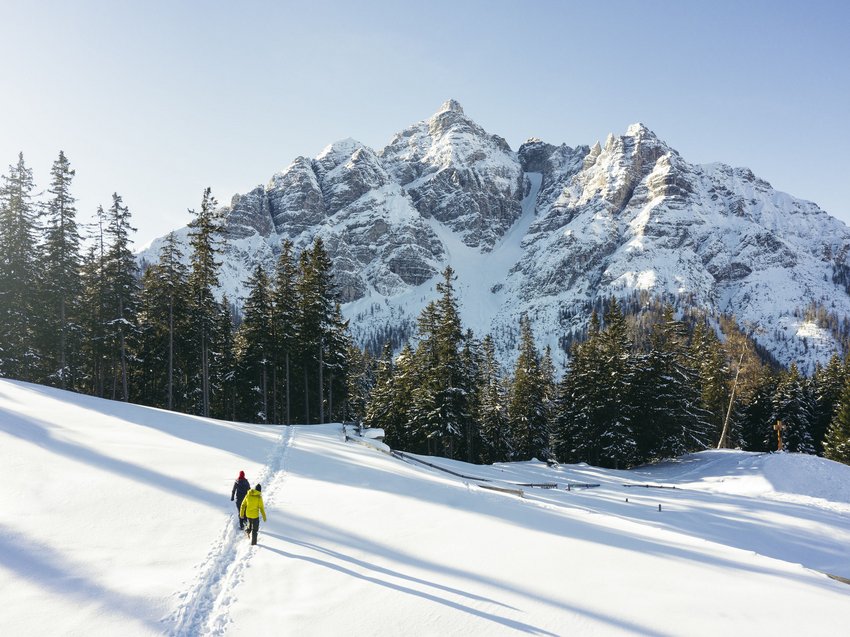 Highlights im Chalet in den Bergen Zwei Wanderer im Schnee wandern auf Pfad vor schneebedeckten Bergen und Tannen