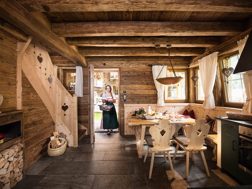Ab ins Luxus-Chalet in Tirol Holzinneneinrichtung in einer Berghütte mit traditionell gekleideter Frau im Türrahmen