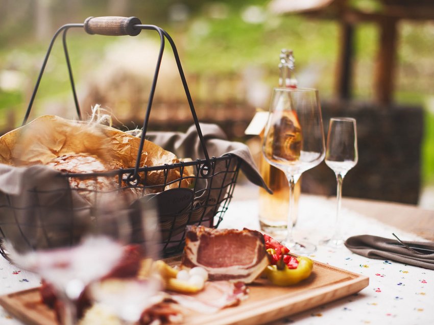Ab ins Chalet mit Hund in Österreich Brotkorb, Aufschnitt und Wein auf einem gedeckten Tisch im Freien