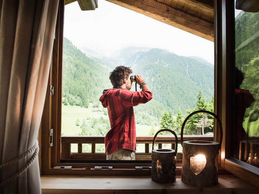 Your luxury chalet in Tyrol awaits Man on balcony using binoculars looking at green mountain landscape