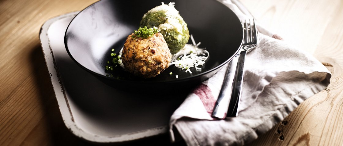 Culinary indulgence all across Stubaital Two stuffed dumplings on black plate with cutlery on wooden table