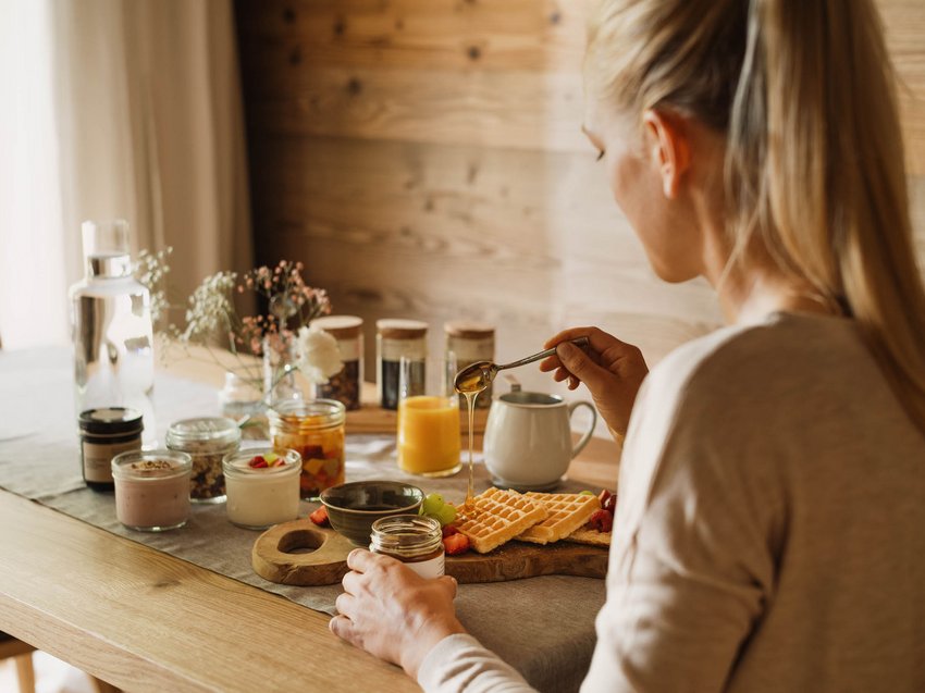 Informationen von A bis Z Frau gießt Honig auf Waffeln an einem Tisch mit Frühstückszutaten