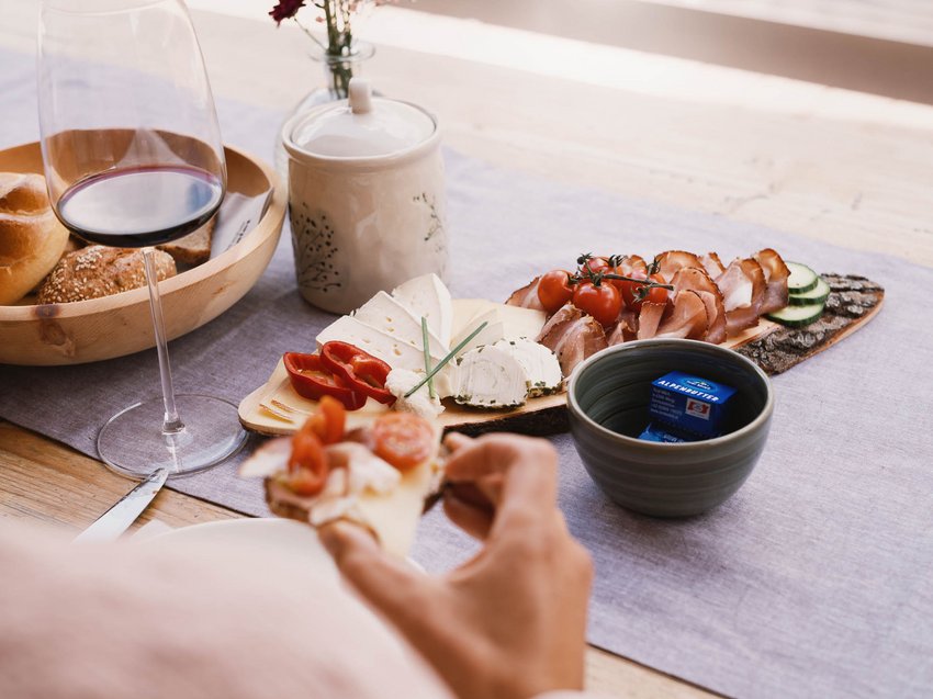 Culinary indulgence all across Stubaital Person holding sandwich in front of cheese, meat, bread platter and a glass of red wine