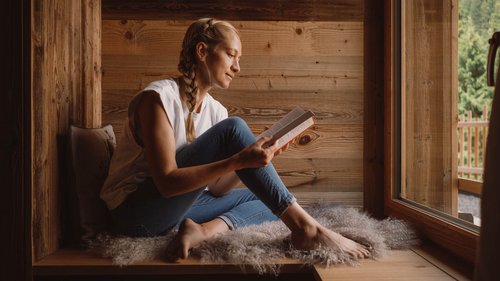 Enquire about your chalet holiday now! Woman sitting relaxed by the window reading a book in a wooden cabin