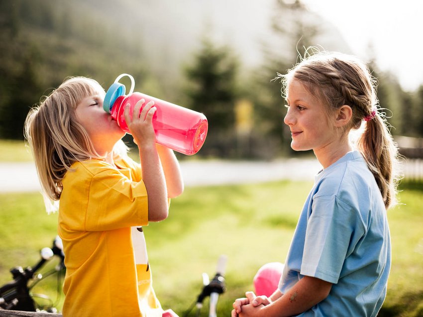 Ein unvergesslicher Sommerurlaub im Stubaital Kind in gelbem Shirt trinkt Wasser, anderes Kind sieht zu im Park
