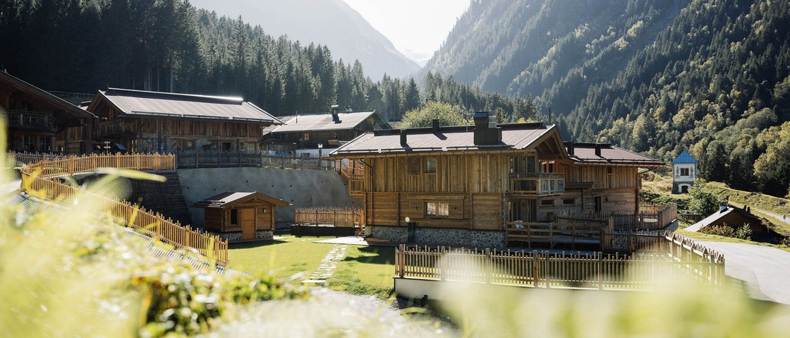 Warum Urlaub im Gletscher Chalet im Stubaital? Holzhäuser in einem sonnigen Tal mit Bergen und Wald im Hintergrund