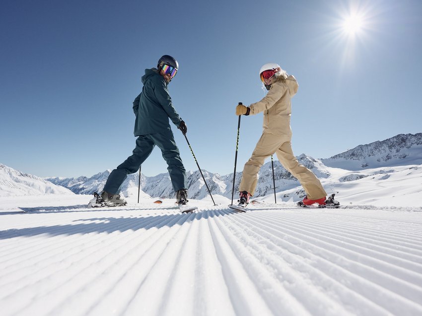 Ab ins Luxus-Chalet in Tirol Zwei Skifahrer in Winterkleidung auf frisch präparierter Piste in den Bergen bei Sonnenschein