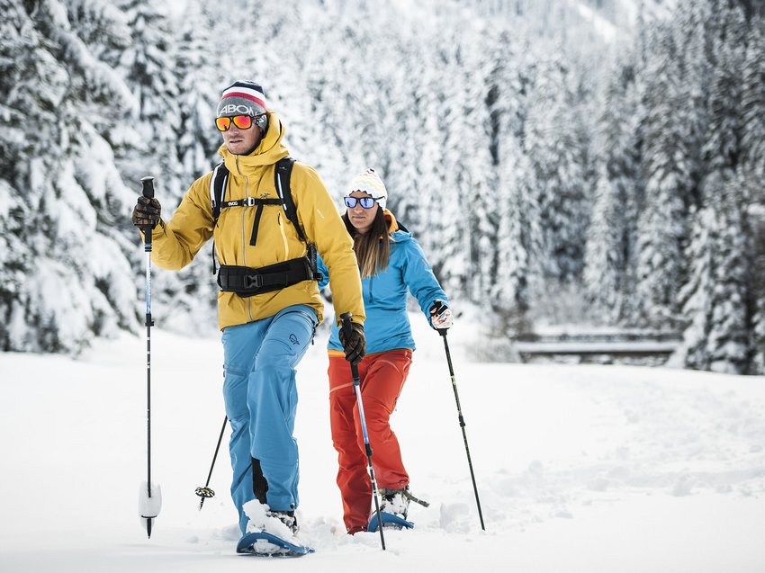 Ab ins Chalet mit Hund in Österreich Zwei Personen machen Schneeschuhwandern im verschneiten Wald