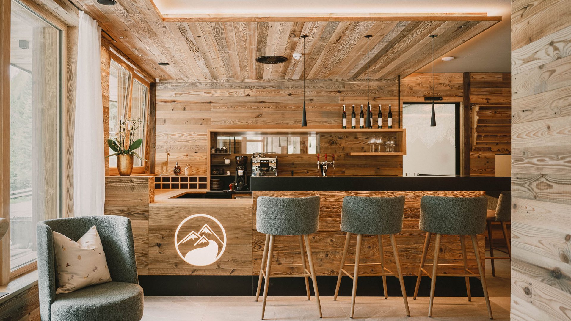 Get away from it all and relax at our chalet in Stubaital Modern wooden bar area with stools, armchair, and decorative mountain logo
