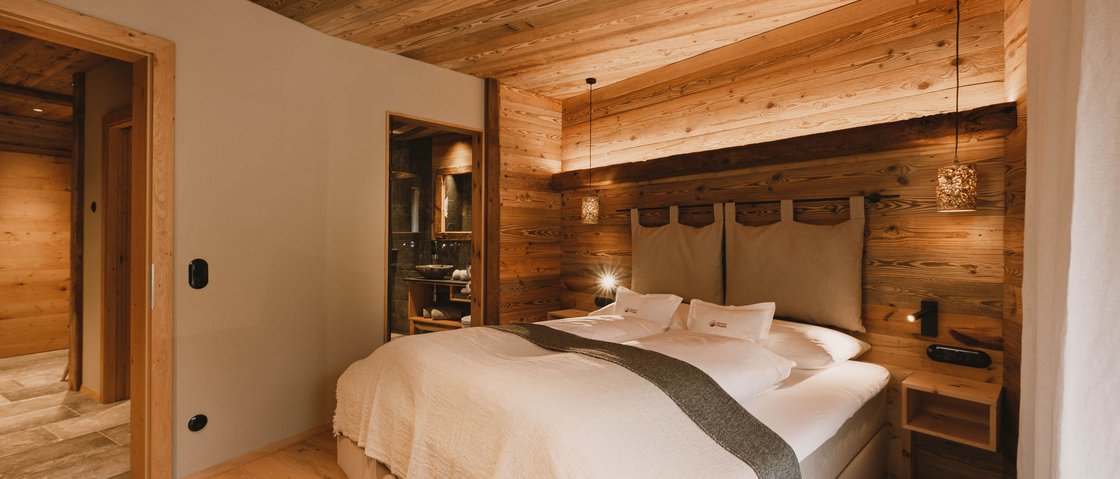 Warum Urlaub im Gletscher Chalet im Stubaital? Gemütliches Schlafzimmer mit Holzwänden und großem Bett in warmem Licht