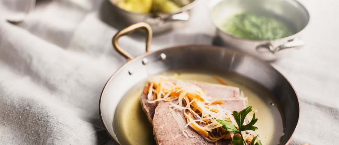 Culinary indulgence all across Stubaital Plate with boiled meat, vegetables, and broth, side dishes in bowls in the background