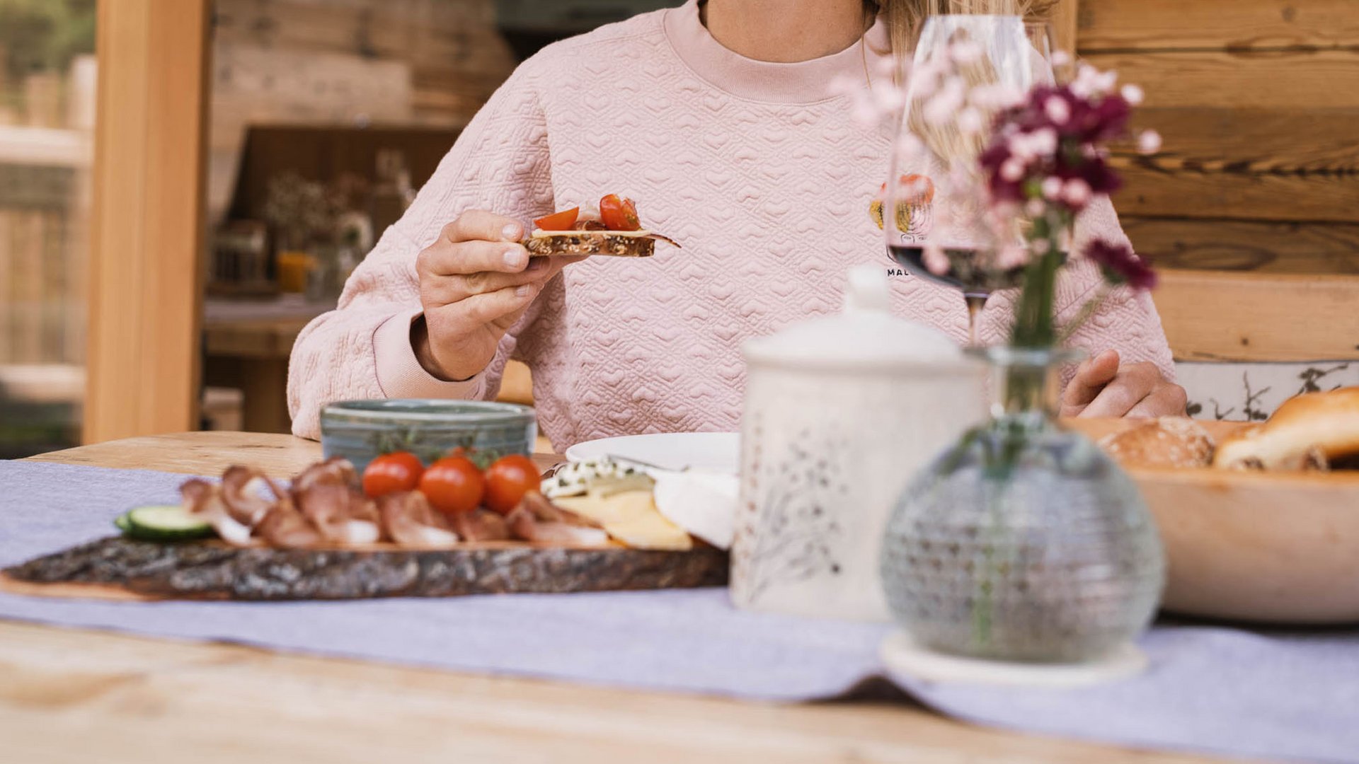 Frau isst Brot mit Tomaten an einem Holztisch mit Snacks und Dekoration