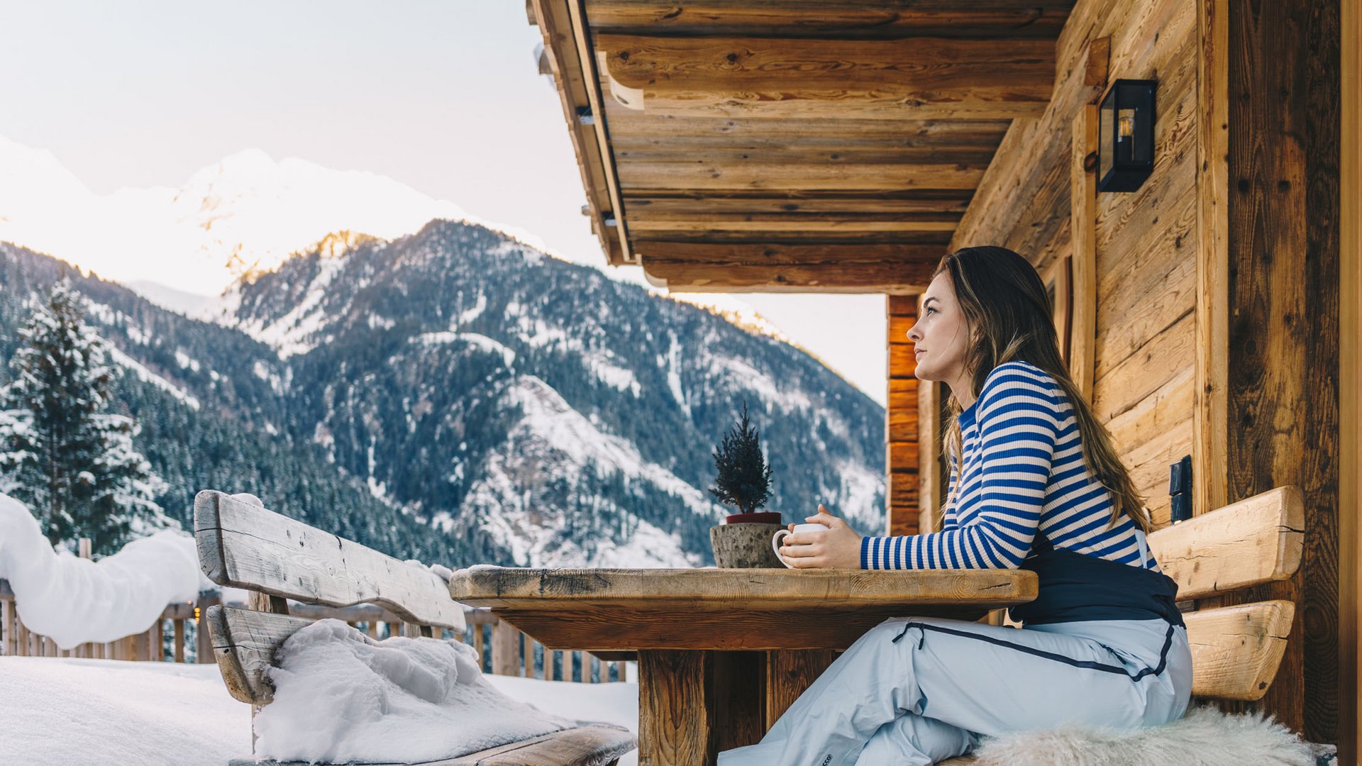 Woman sitting with cup on wooden balcony overlooking snowy mountains